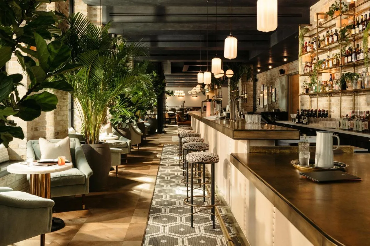 a bar with a row of bar stools and plants at The Hoxton, Southwark in London